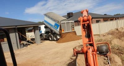 White truck tipping trailer filled with dirt onto the ground in backyard.